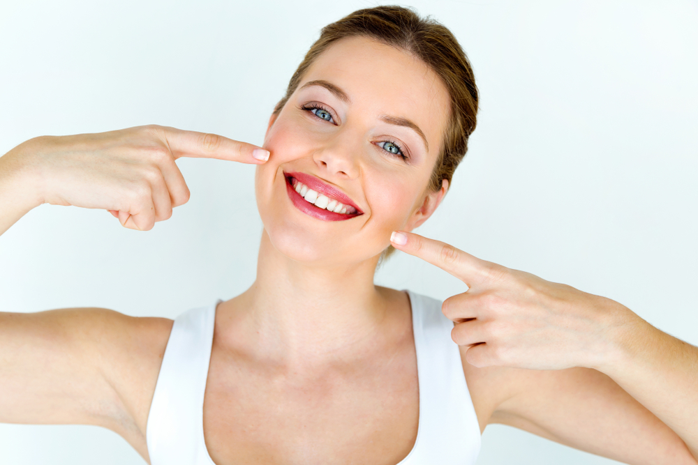 Image of a smiling, confident, mature female implant periodontist in a surgical gown, holding a dental implant model, in a modern dental office. No text on image.